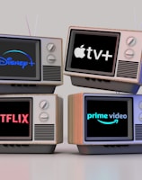 Four old-style television sets are stacked in two rows and each screen displays a different streaming service logo: Disney+, Apple TV+, Netflix, and Prime Video.